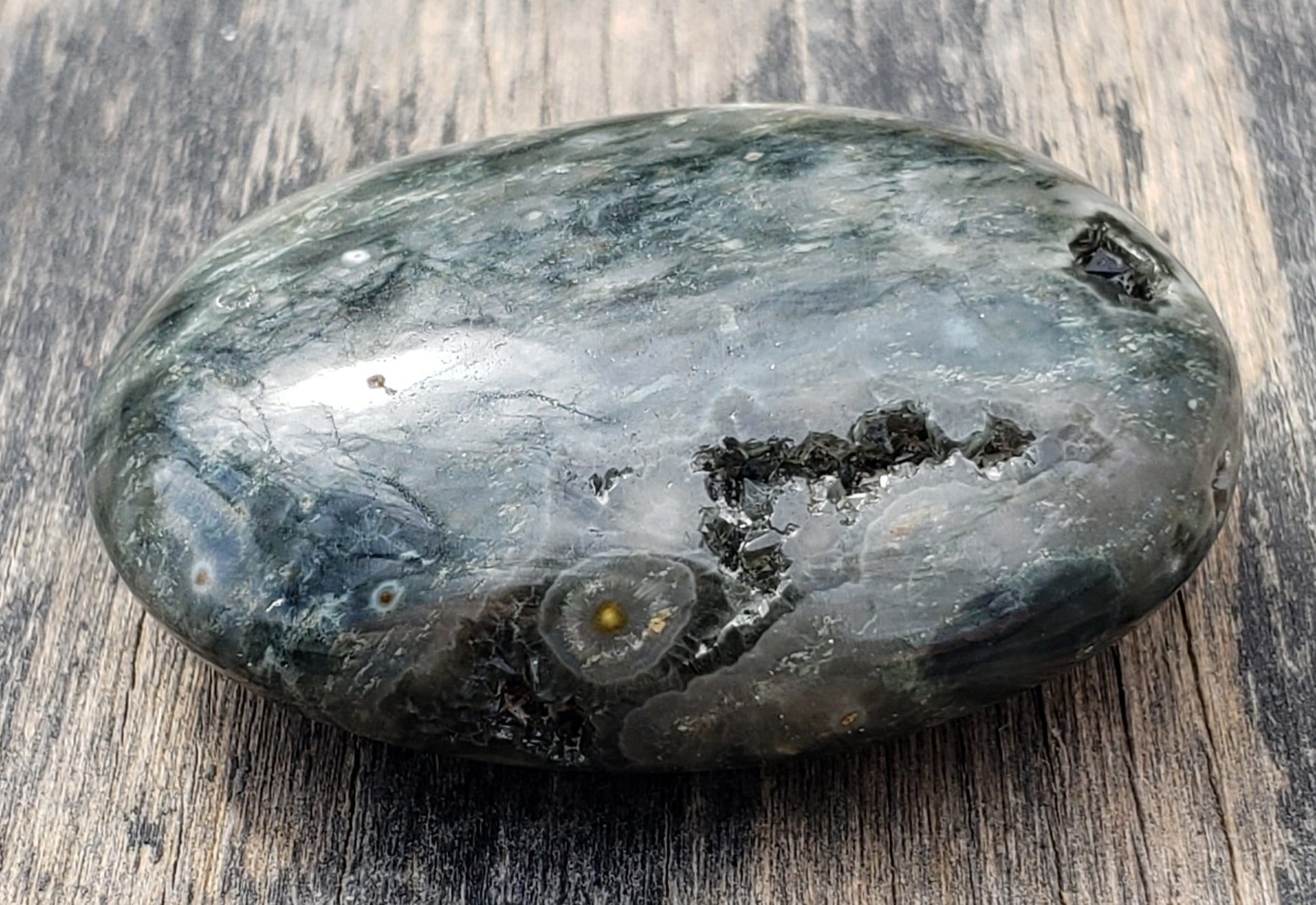 A polished Ocean Jasper palm stone with visible green color and natural patterns, containing a druzy vug. PS08-2