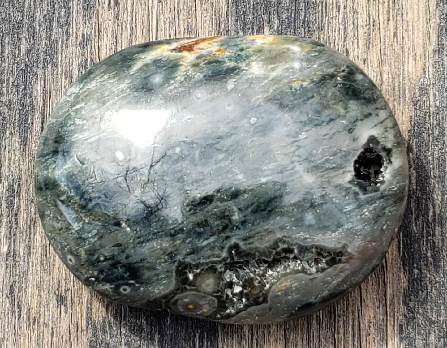 A polished Ocean Jasper palm stone with visible green color and natural patterns, containing a druzy vug. PS08-1