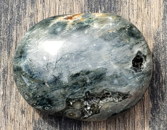 A polished Ocean Jasper palm stone with visible green color and natural patterns, containing a druzy vug. PS08-1