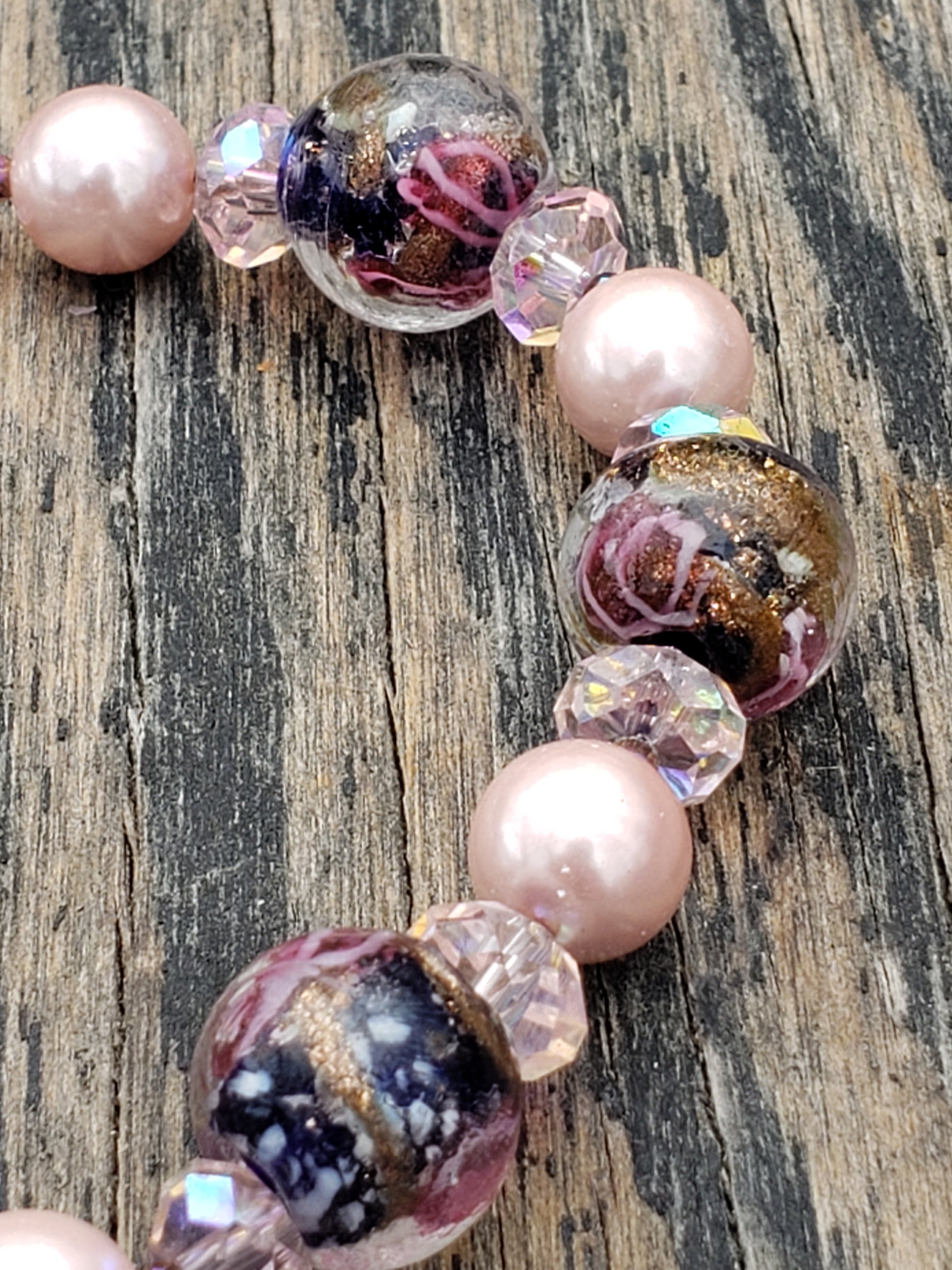 Close-up of a glass beaded bracelet with pink, dark blue, and copper colors, featuring flower patterns and round beads, fastened with a silver clasp.
