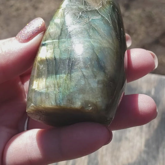 Polished labradorite freeform crystal showing bright golden flash with subtle blue and green tones in natural light video ff03