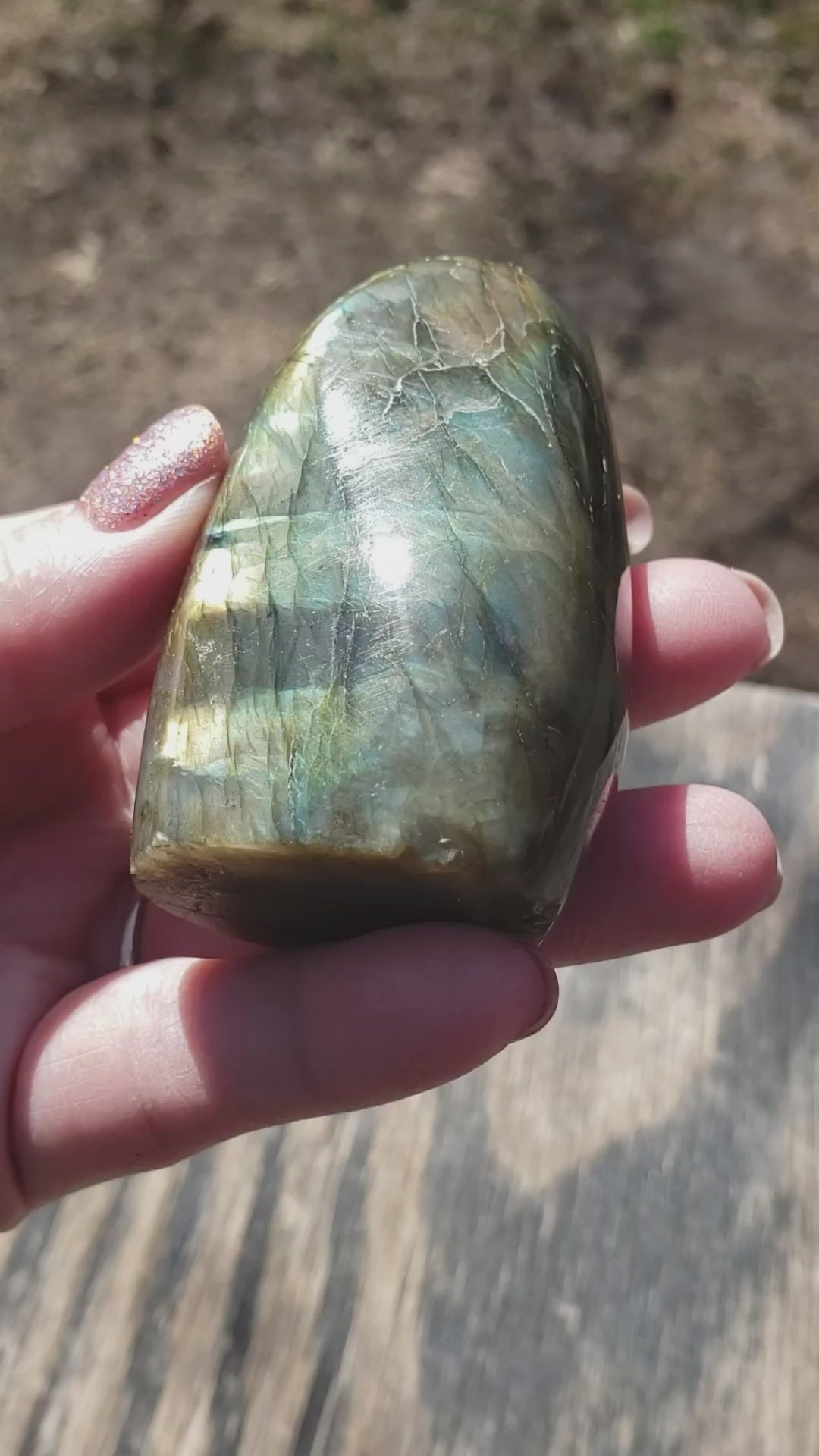 Polished labradorite freeform crystal showing bright golden flash with subtle blue and green tones in natural light video ff03