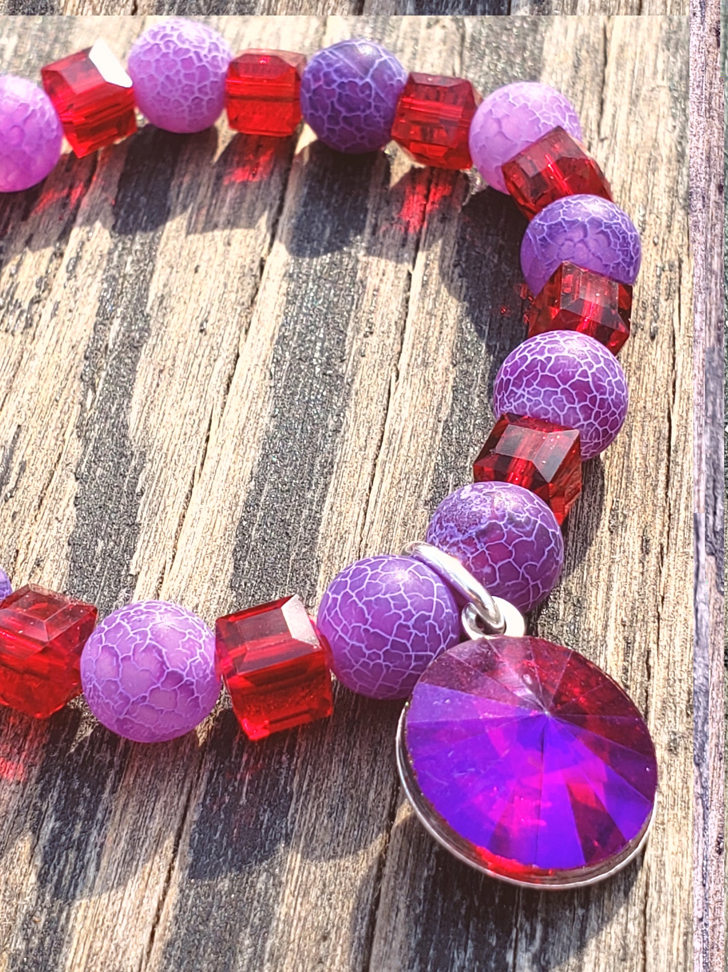 A stretch bracelet with a mix of purple agate beads, red glass beads, and a large red purple glass super sparkle charm